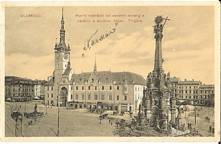 Tahle fotografie, respektive pohlednice, je ještě o rok starší, pochází z roku 1913 a zachycuje klasický olomoucký námět: Trojici s radnicí. Všimněte si fasády čelní strany radnice! 
Neznámý pisatel připojil vlastenecký pozdrav Nazdar. Zdalipak víte, jak se tahle dnes už typická zdravice zrodila? Kdo nám nejrychleji pošle správnou odpověď na adresu redakce@olomouc.cz, má u nás volňásek do Premiere Cinemas. (Soutěž už má výherkyni, je jí Zuzana Koutná)